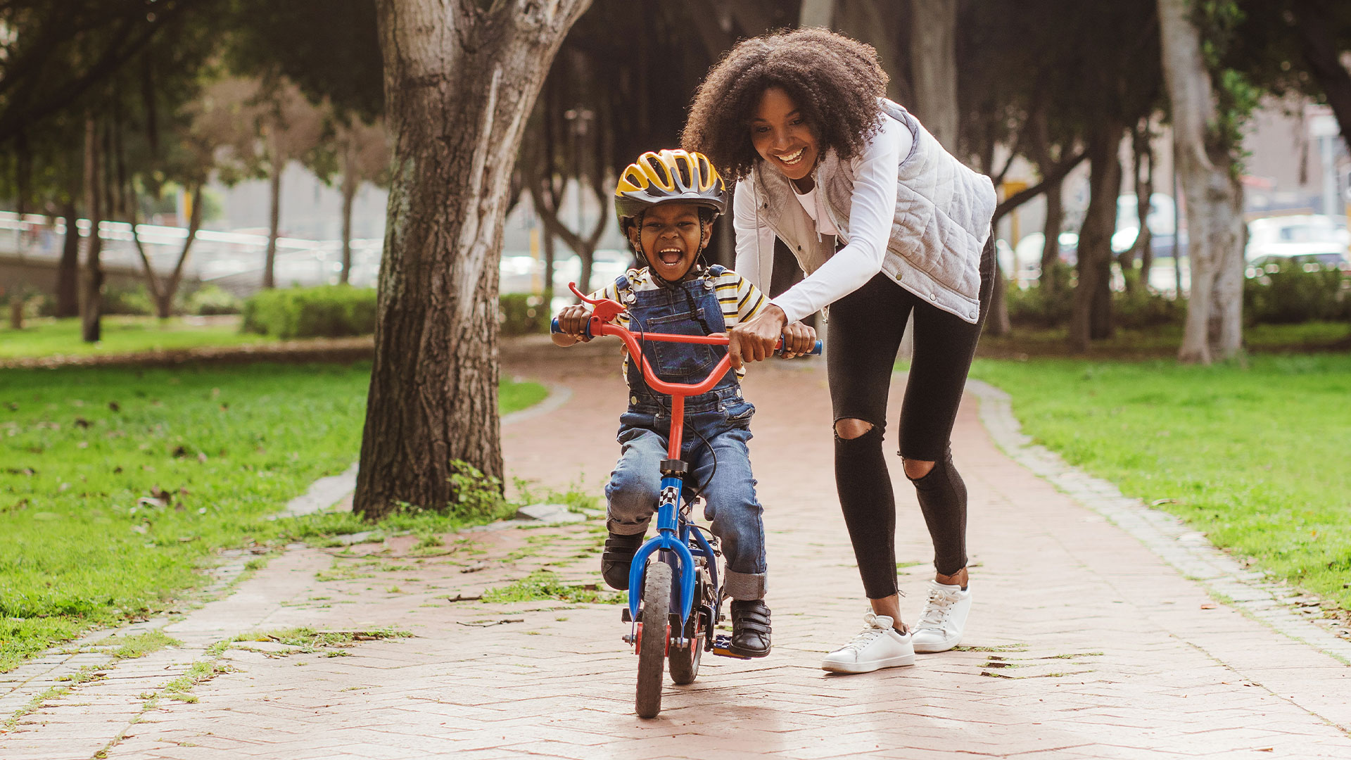 A little boy riding a bike thats being held steady by his mother