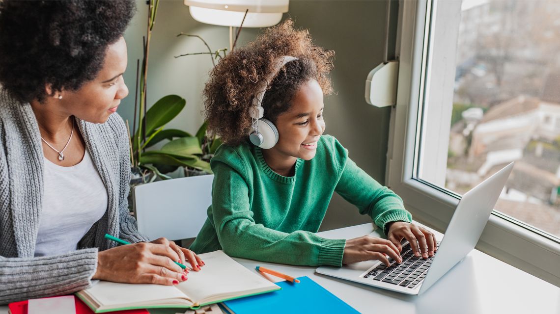 Young person and adult looking from paper-based notes towards a laptop